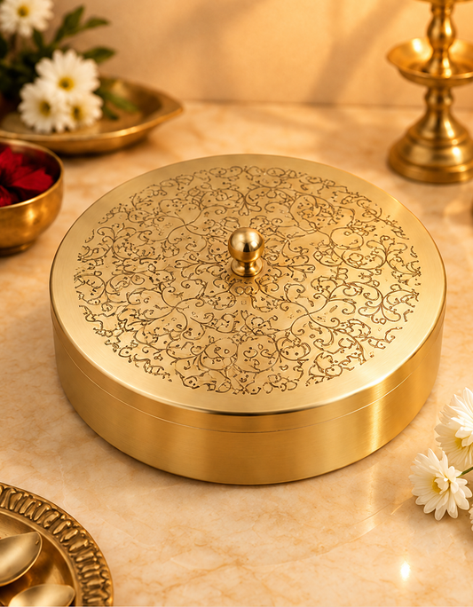 Engraved brass masala dabba with floral lid on a marble kitchen counter